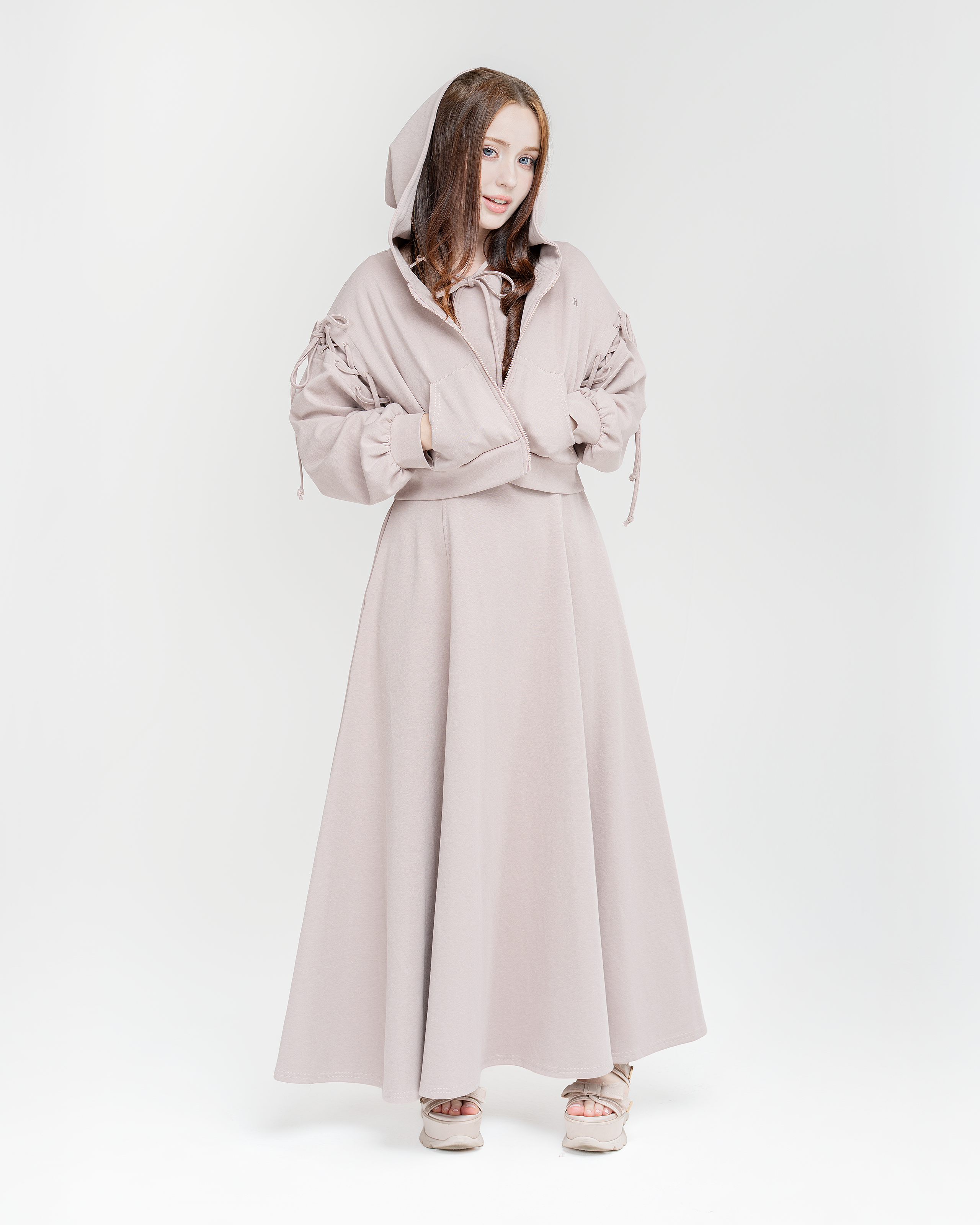 Woman wearing a hoodie with bows and a dusty rose long dress on a white background
