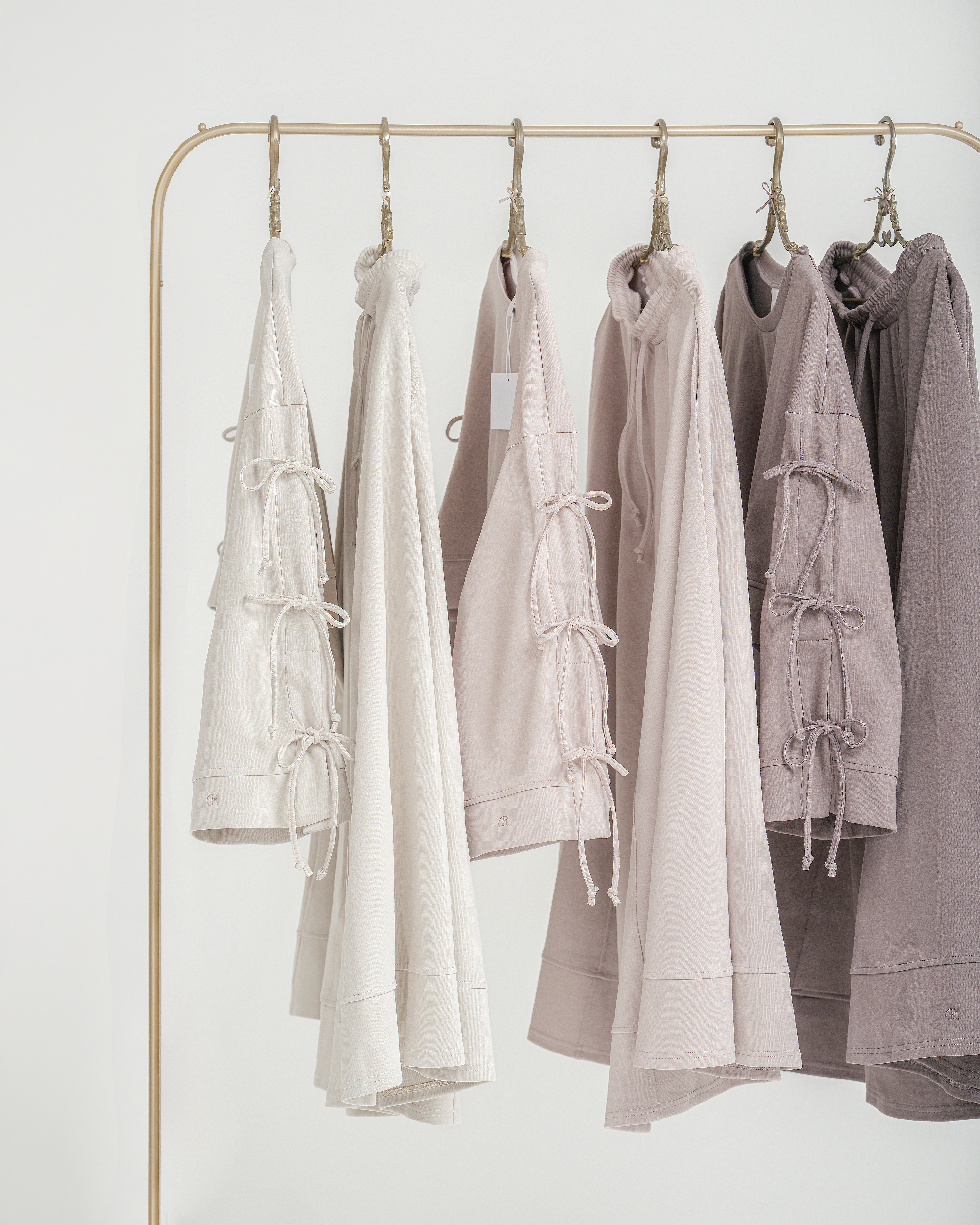Collection of light-colored clothing from Dustyrosa on a gold rack against a white background