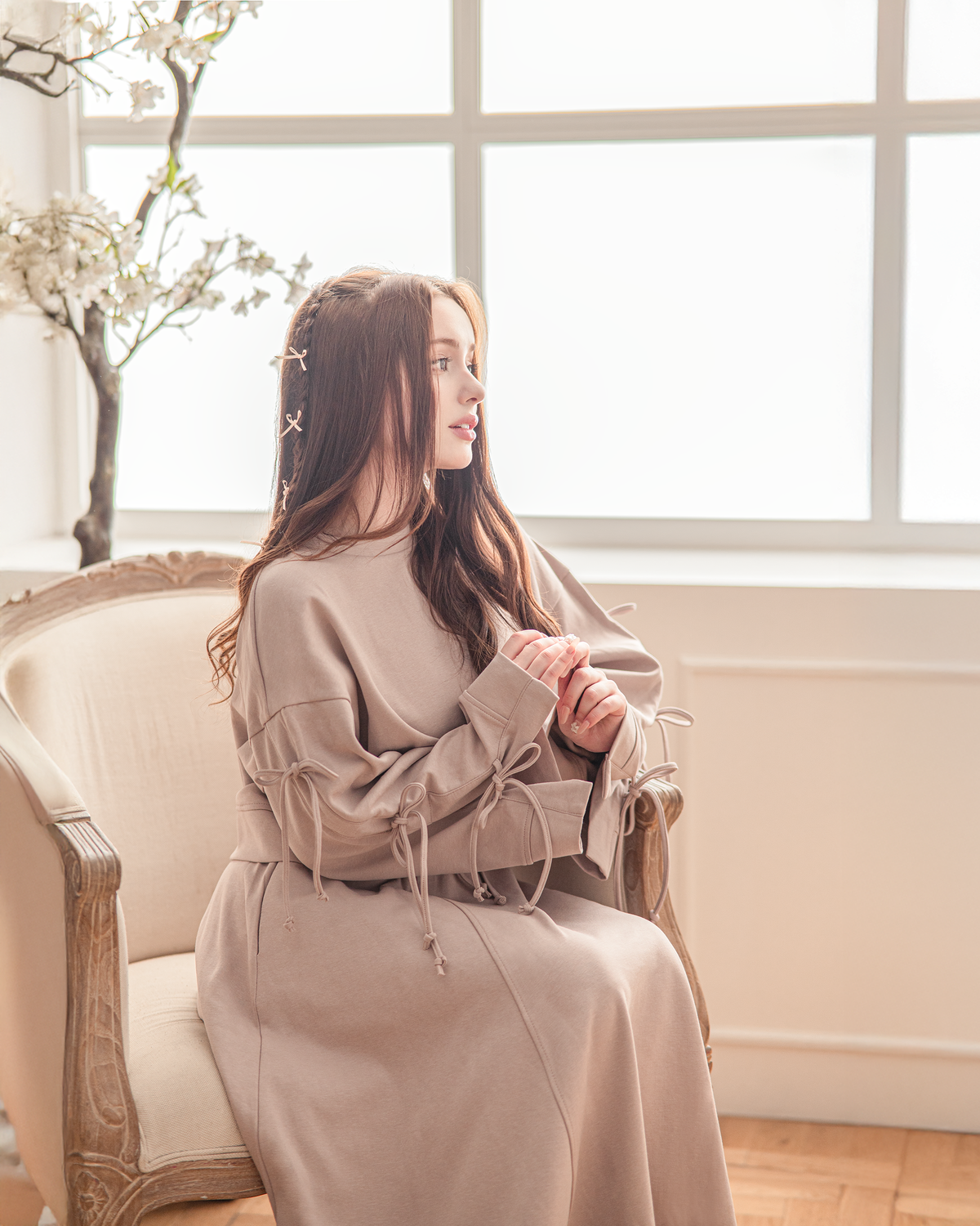 Reverie set in dusty rose, seated by a window in a bright room.